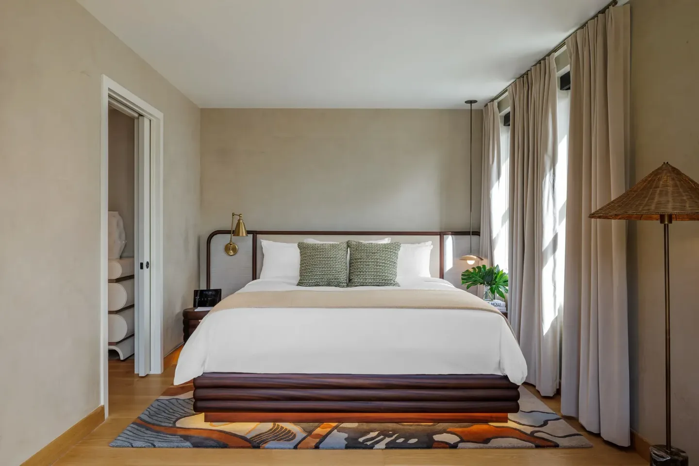 A king bed with layered neutral linens in a light-filled suite bedroom with tall windows